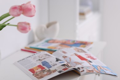 Photo of Many different trendy magazines and tulip flowers on white cabinet indoors, closeup