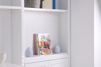 Photo of Many different trendy magazines and vases in white shelving unit indoors