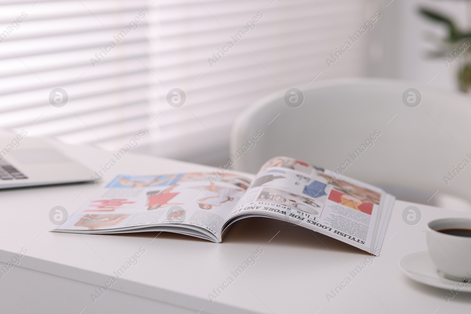 Photo of Open trendy magazine, laptop and coffee on white table indoors, closeup