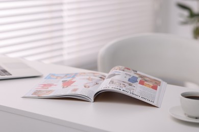 Photo of Open trendy magazine, laptop and coffee on white table indoors, closeup