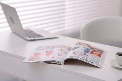 Photo of Open trendy magazine, laptop and coffee on white table indoors, closeup