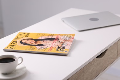Photo of Trendy magazine, laptop and coffee on white table indoors, closeup