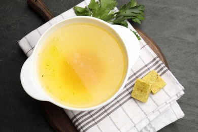 Photo of Aromatic bouillon cubes, broth and parsley on black table, top view