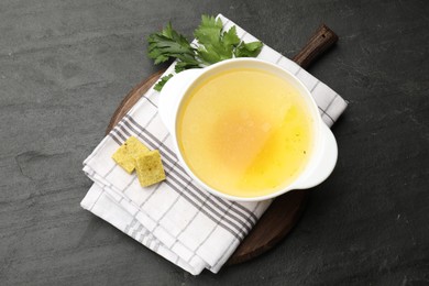 Photo of Aromatic bouillon cubes, broth and parsley on black table, top view