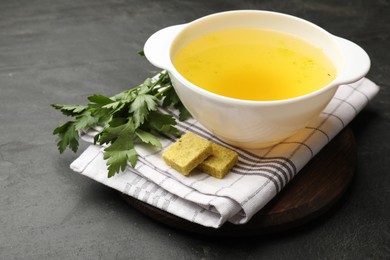 Photo of Aromatic bouillon cubes, broth and parsley on black table, closeup