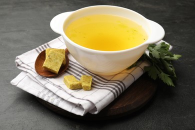 Photo of Aromatic bouillon cubes, broth and parsley on black table, closeup