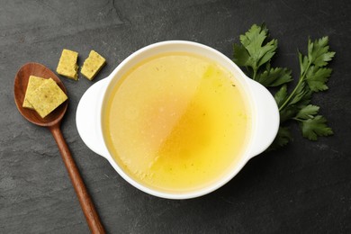 Photo of Aromatic bouillon cubes, broth and parsley on black table, flat lay