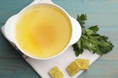 Photo of Aromatic bouillon cubes, broth and parsley on light blue wooden table, flat lay