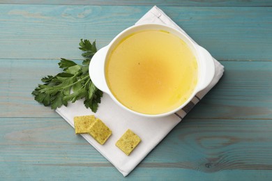 Photo of Aromatic bouillon cubes, broth and parsley on light blue wooden table, flat lay