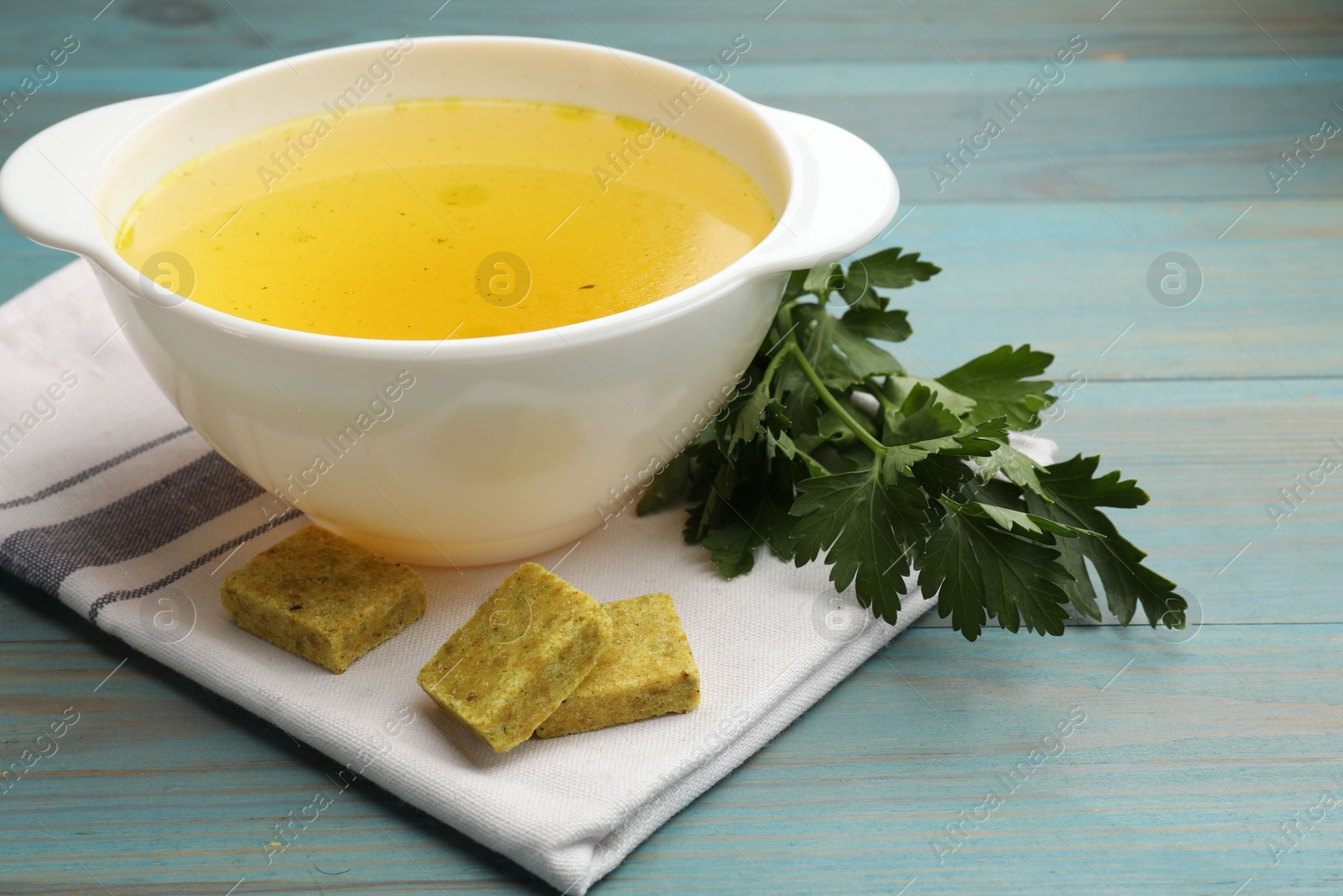 Aromatic bouillon cubes, broth and parsley on light blue wooden table, closeup Photo of Aromatic bouillon cubes, broth and parsley on light blue wooden table, closeup