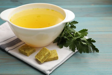 Photo of Aromatic bouillon cubes, broth and parsley on light blue wooden table, closeup