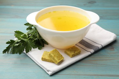 Photo of Aromatic bouillon cubes, broth and parsley on light blue wooden table, closeup