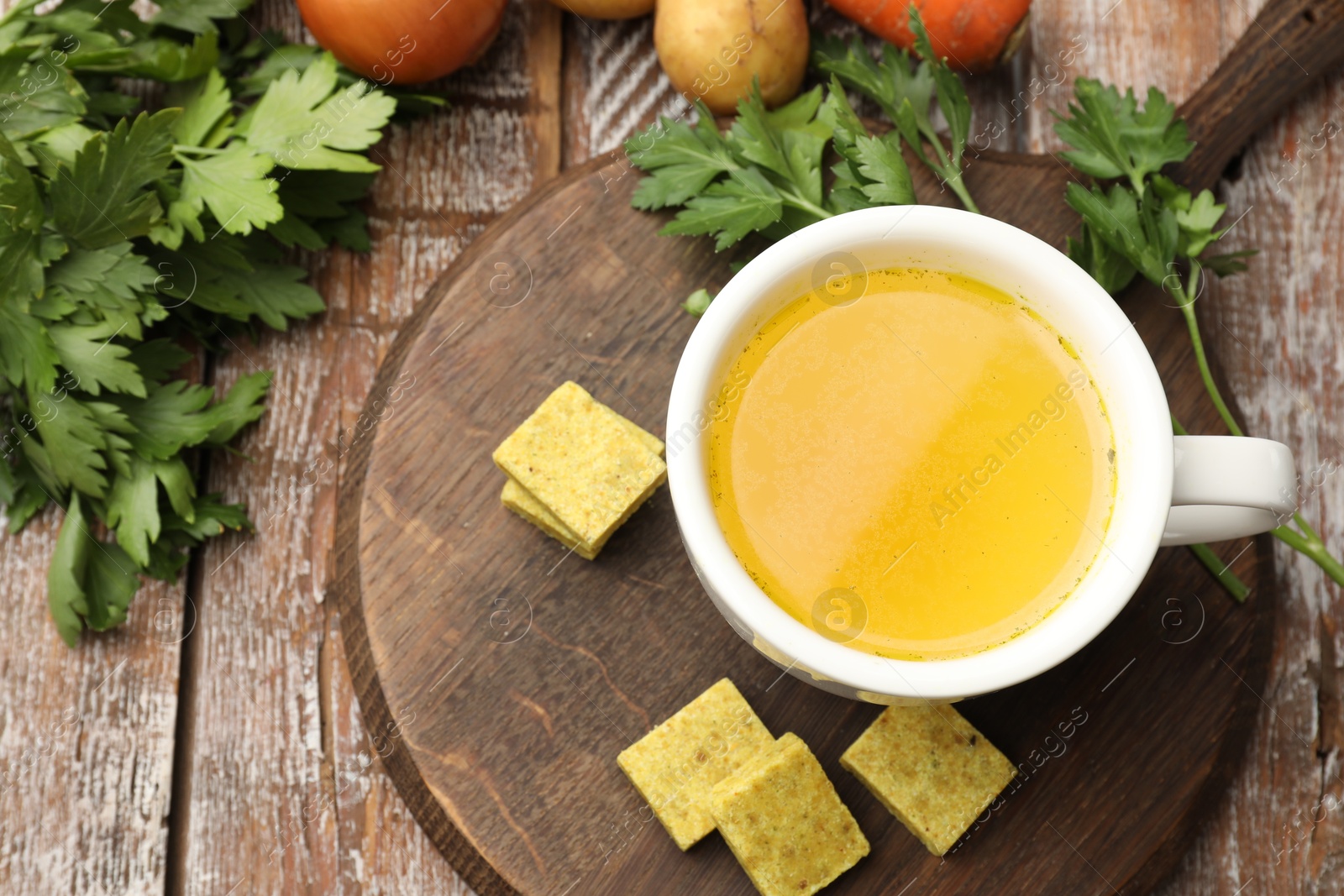 Aromatic bouillon cubes, broth, parsley and vegetables on wooden table, flat lay Photo of Aromatic bouillon cubes, broth, parsley and vegetables on wooden table, flat lay