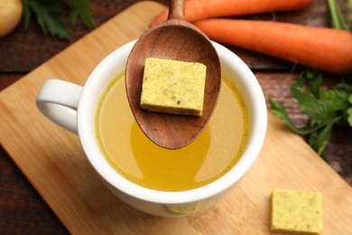 Photo of Putting aromatic bouillon cube into broth at wooden table, above view