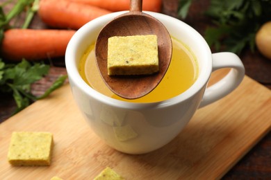 Photo of Putting aromatic bouillon cube into broth at table, closeup