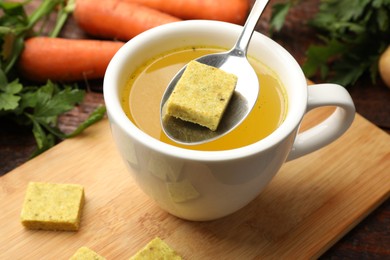 Photo of Putting aromatic bouillon cube into broth at table, closeup
