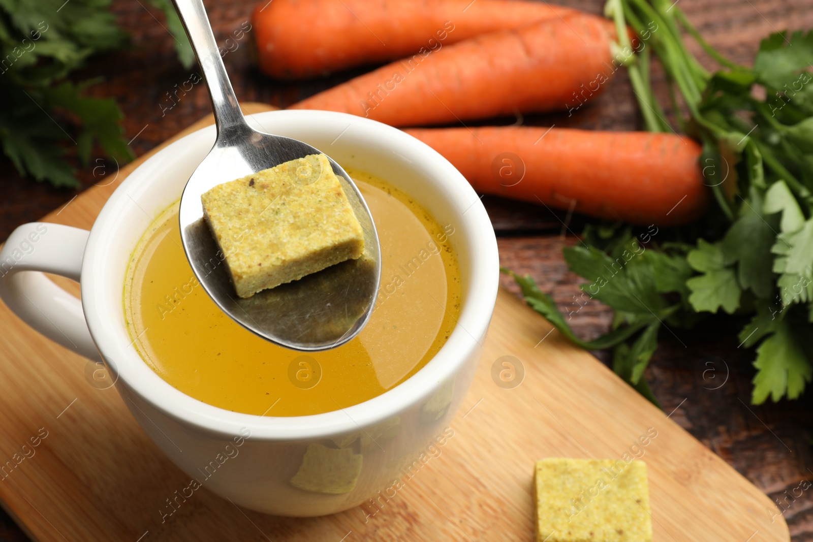Photo of Putting aromatic bouillon cube into broth at wooden table, above view