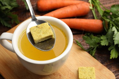Photo of Putting aromatic bouillon cube into broth at wooden table, above view