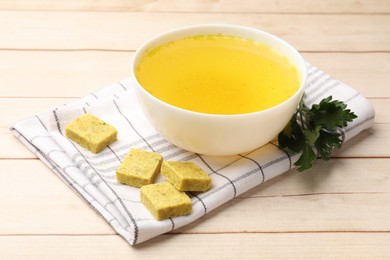 Photo of Aromatic bouillon cubes, broth and parsley on wooden table, closeup