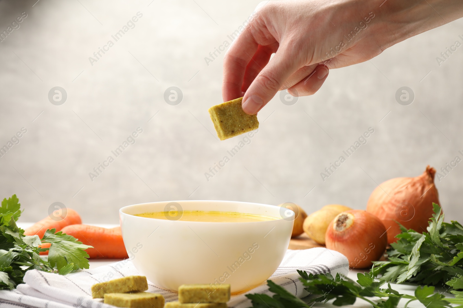 Woman putting aromatic bouillon cube into broth at table, closeup Photo of Woman putting aromatic bouillon cube into broth at table, closeup