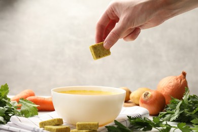Photo of Woman putting aromatic bouillon cube into broth at table, closeup