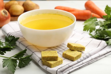 Photo of Aromatic bouillon cubes, broth, parsley and vegetables on white table, closeup