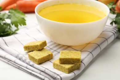 Photo of Aromatic bouillon cubes, broth, parsley and vegetables on white table, closeup