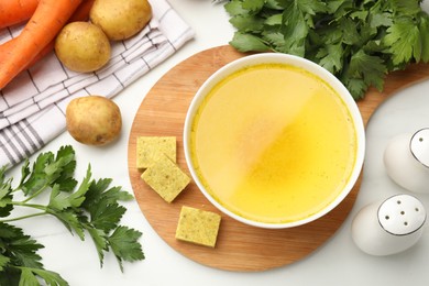 Photo of Aromatic bouillon cubes, broth, parsley and vegetables on white marble table, flat lay