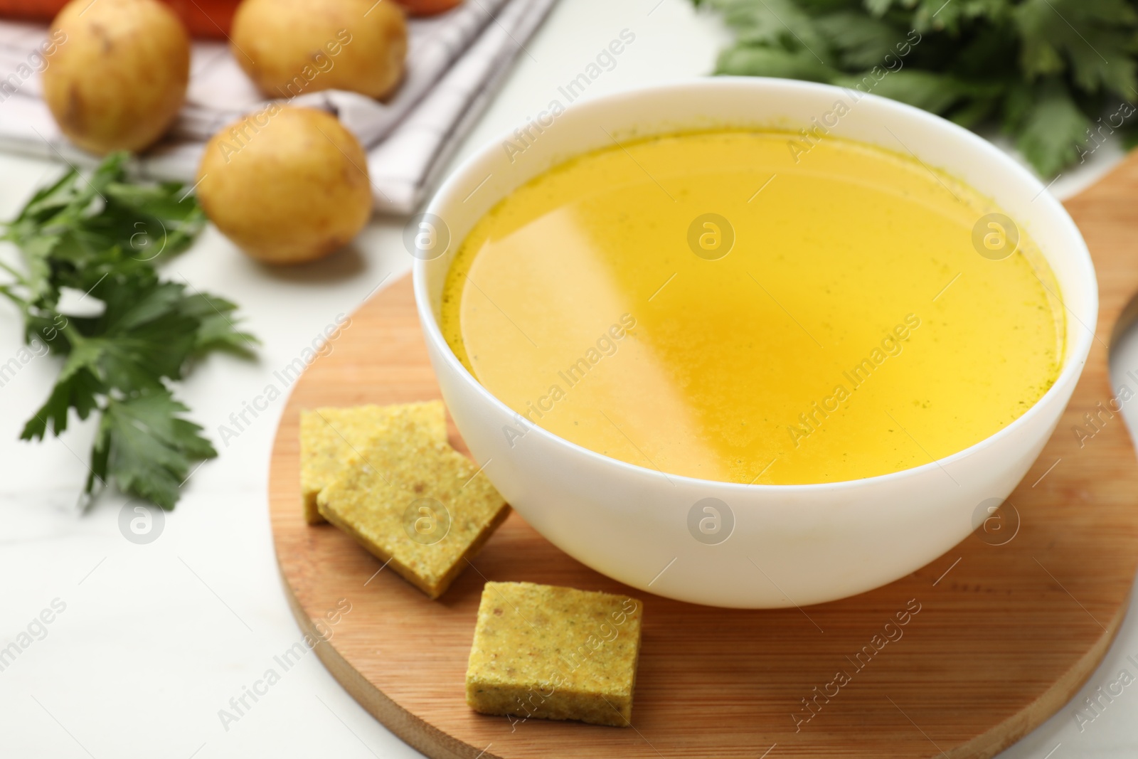 Aromatic bouillon cubes, broth, parsley and vegetables on white table, closeup Photo of Aromatic bouillon cubes, broth, parsley and vegetables on white table, closeup