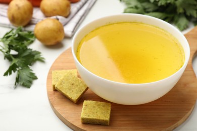 Photo of Aromatic bouillon cubes, broth, parsley and vegetables on white table, closeup