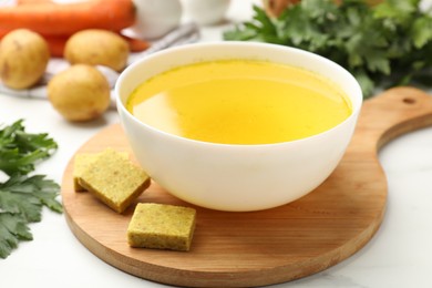 Photo of Aromatic bouillon cubes, broth, parsley and vegetables on white table, closeup