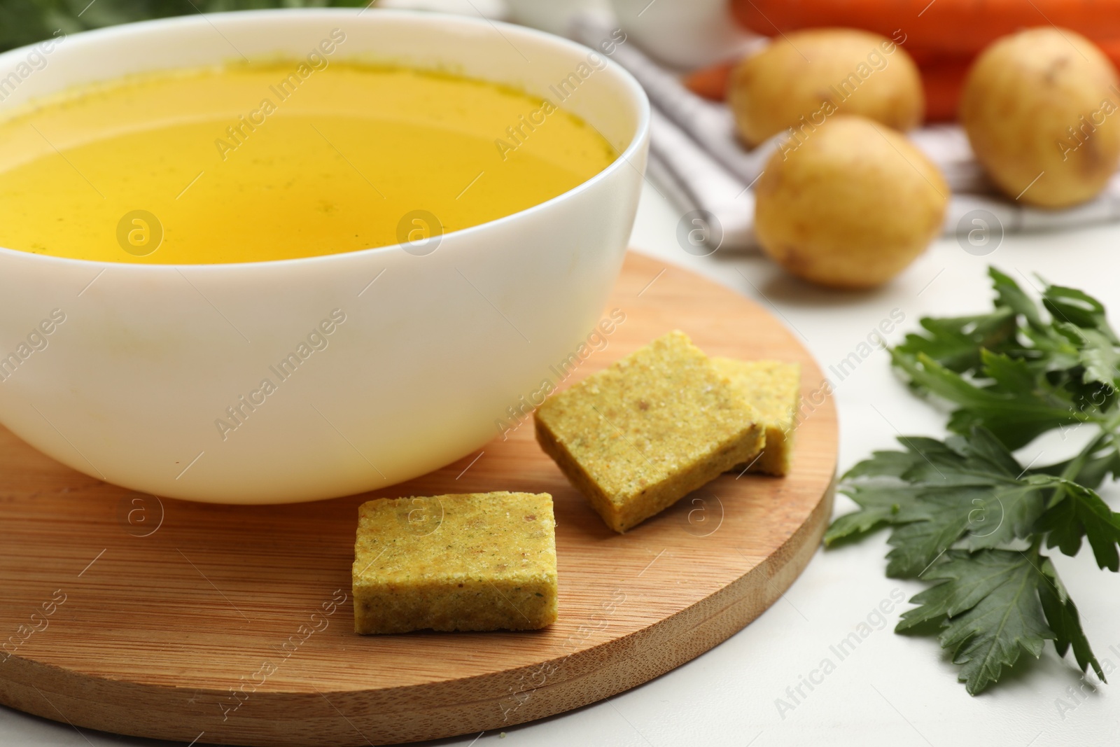 Aromatic bouillon cubes, broth, parsley and vegetables on white table, closeup Photo of Aromatic bouillon cubes, broth, parsley and vegetables on white table, closeup