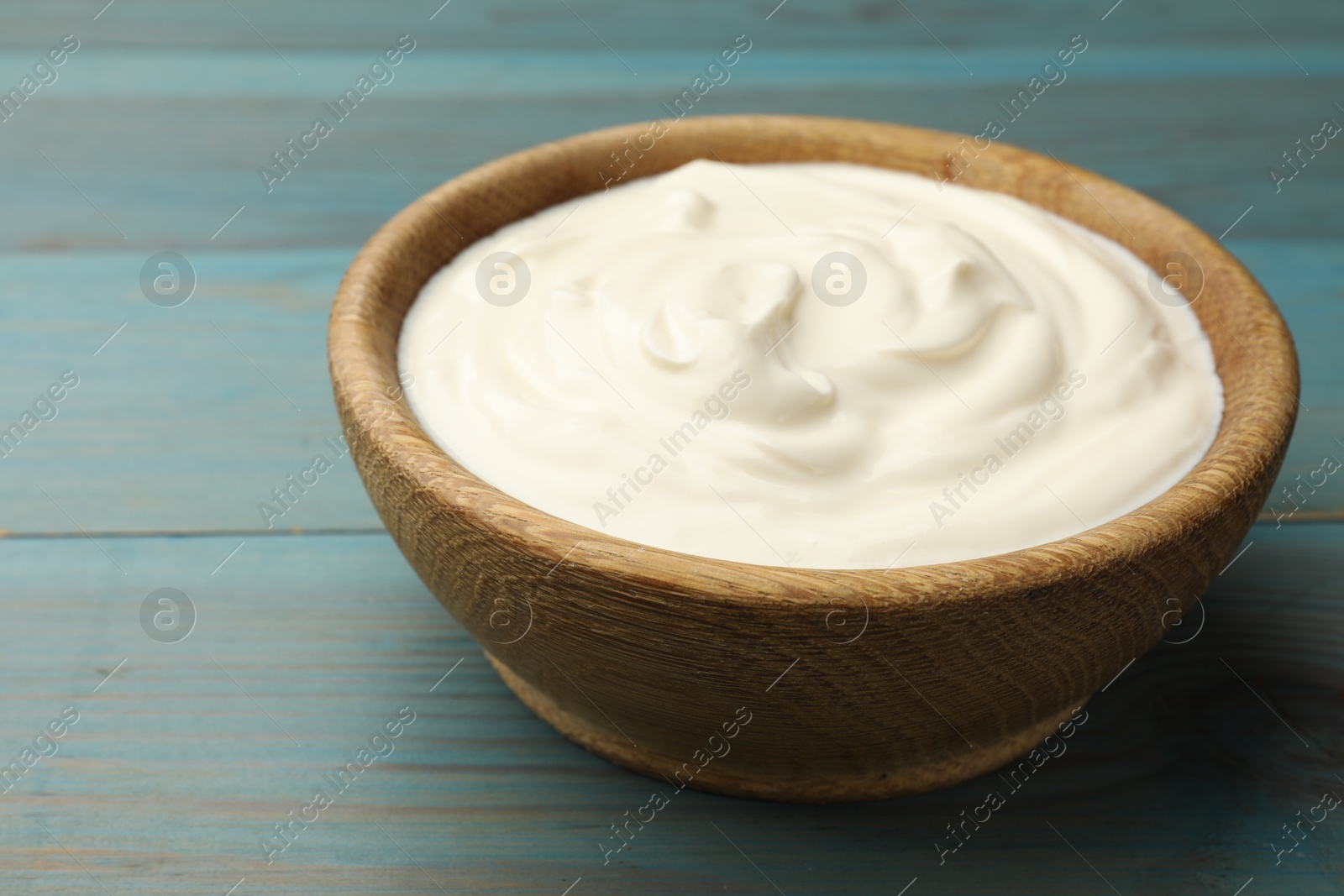 Photo of Tasty sour cream on blue wooden table, closeup