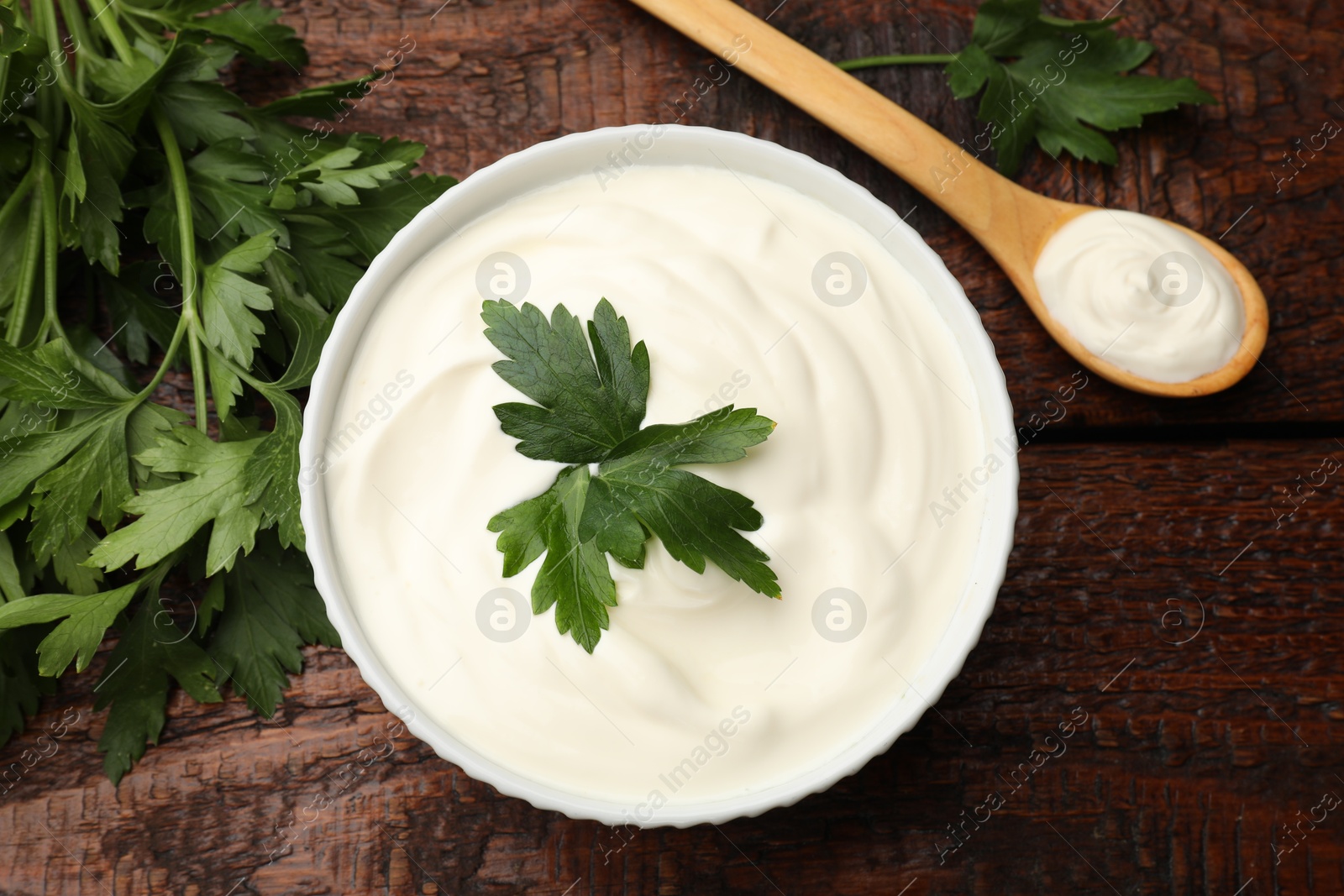 Photo of Tasty sour cream with parsley on wooden table, flat lay