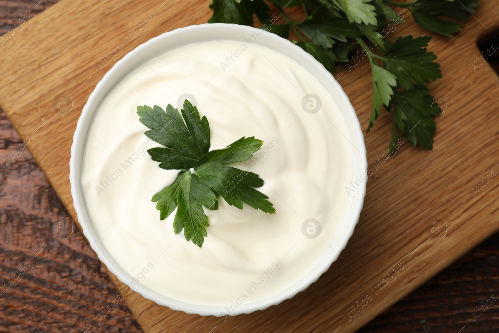Photo of Tasty sour cream with parsley on wooden table, flat lay