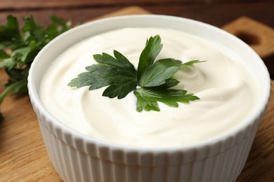 Photo of Tasty sour cream with parsley on wooden table, closeup