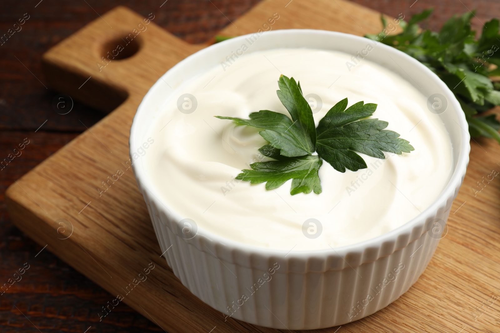 Photo of Tasty sour cream with parsley on wooden table, closeup