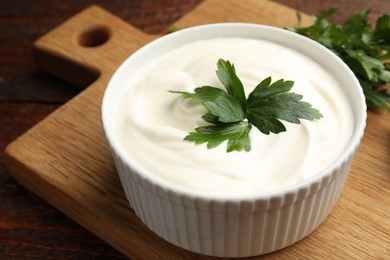 Photo of Tasty sour cream with parsley on wooden table, closeup