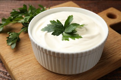 Photo of Tasty sour cream with parsley on wooden table, closeup