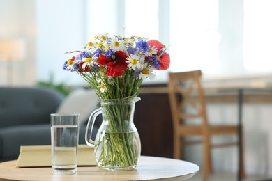 Photo of Beautiful wildflowers in vase, water and book on wooden table at home