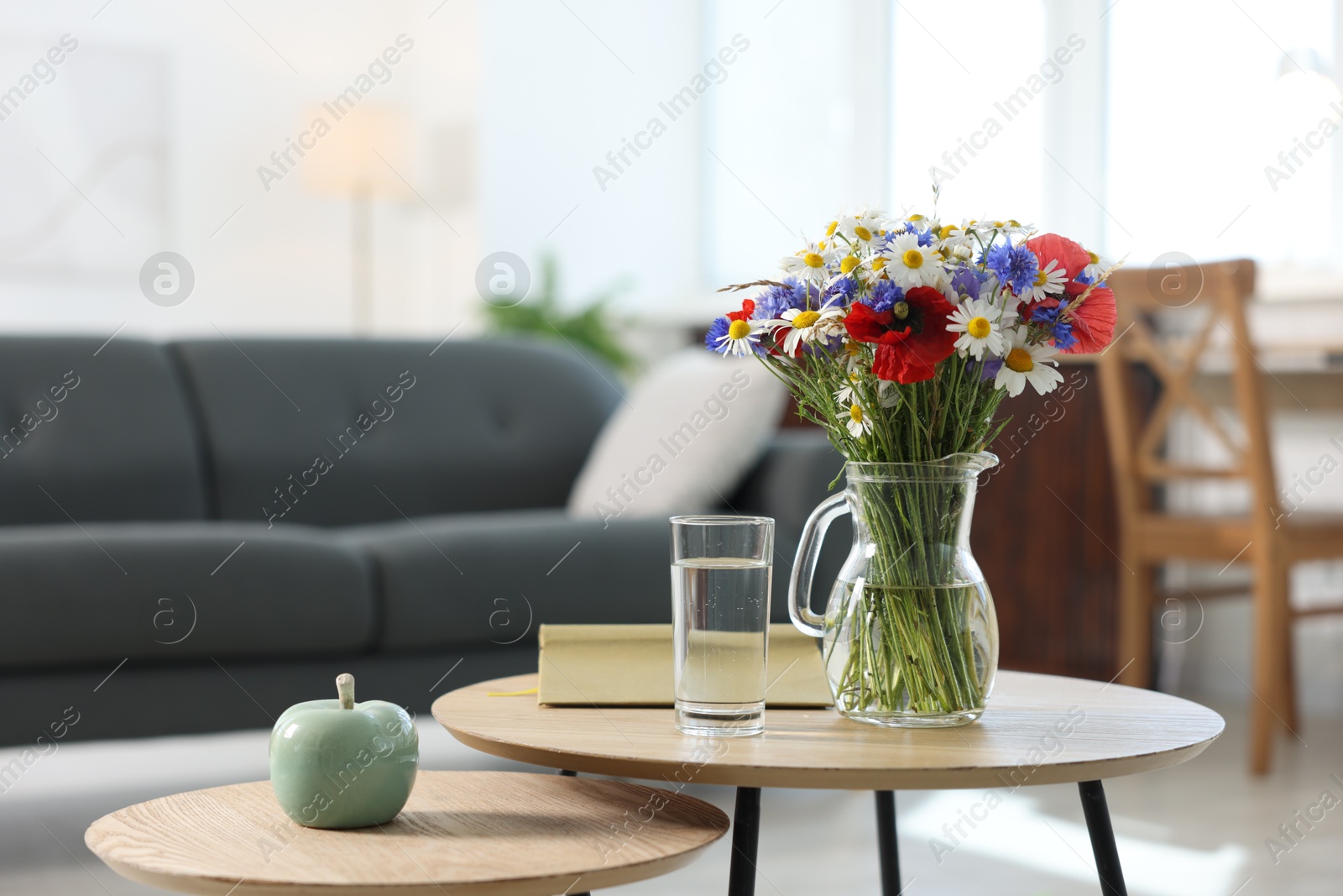 Beautiful wildflowers in vase, water and book on wooden table at home. Space for text Photo of Beautiful wildflowers in vase, water and book on wooden table at home. Space for text
