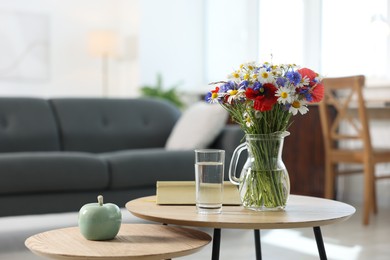 Photo of Beautiful wildflowers in vase, water and book on wooden table at home. Space for text