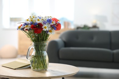 Photo of Beautiful wildflowers in vase and book on wooden table at home. Space for text
