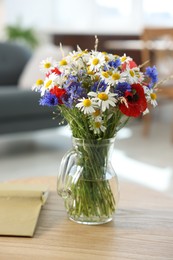 Photo of Beautiful wildflowers in vase and book on wooden table at home