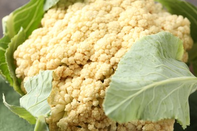Photo of Fresh cauliflower with green leaves as background, closeup