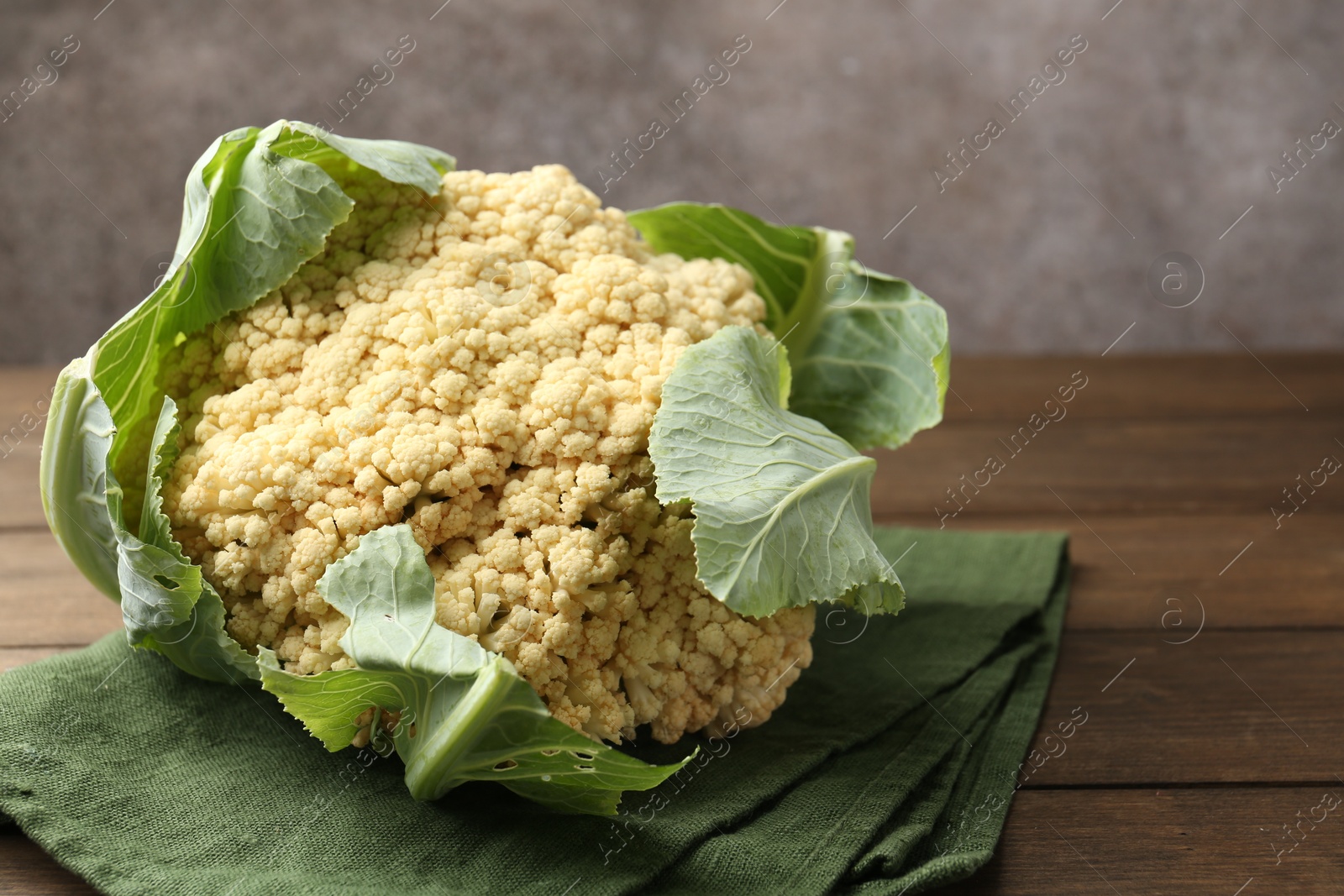 Fresh cauliflower with green leaves on wooden table, closeup. Space for text Photo of Fresh cauliflower with green leaves on wooden table, closeup. Space for text