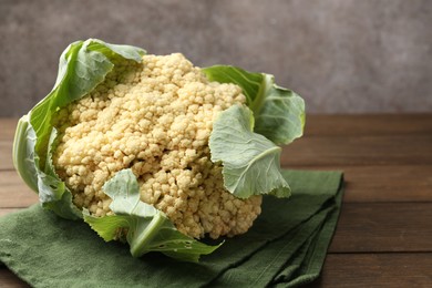 Photo of Fresh cauliflower with green leaves on wooden table, closeup. Space for text