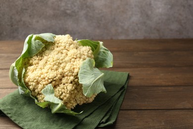 Photo of Fresh cauliflower with green leaves on wooden table, closeup. Space for text