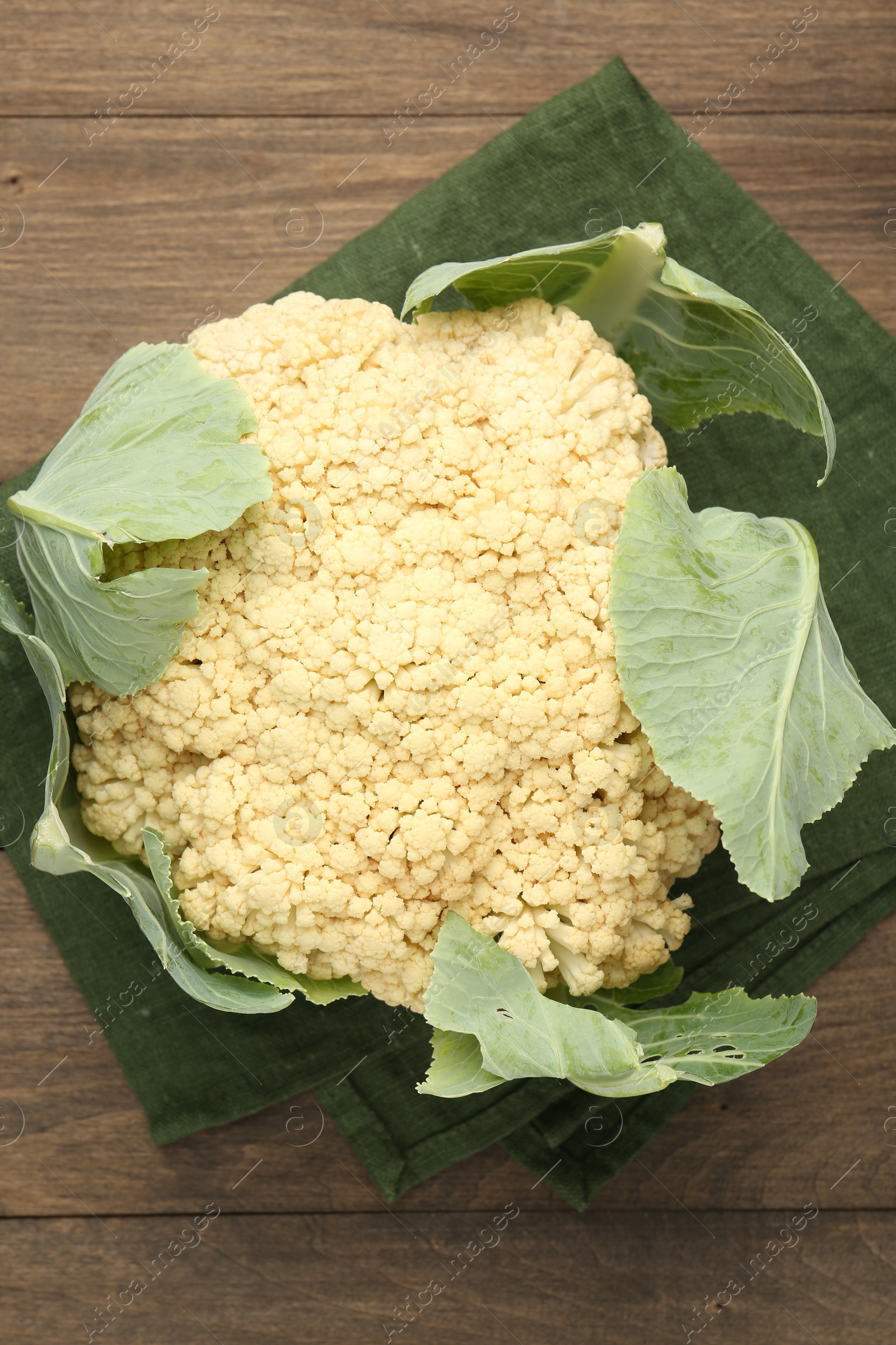Photo of Fresh cauliflower with green leaves on wooden table, top view