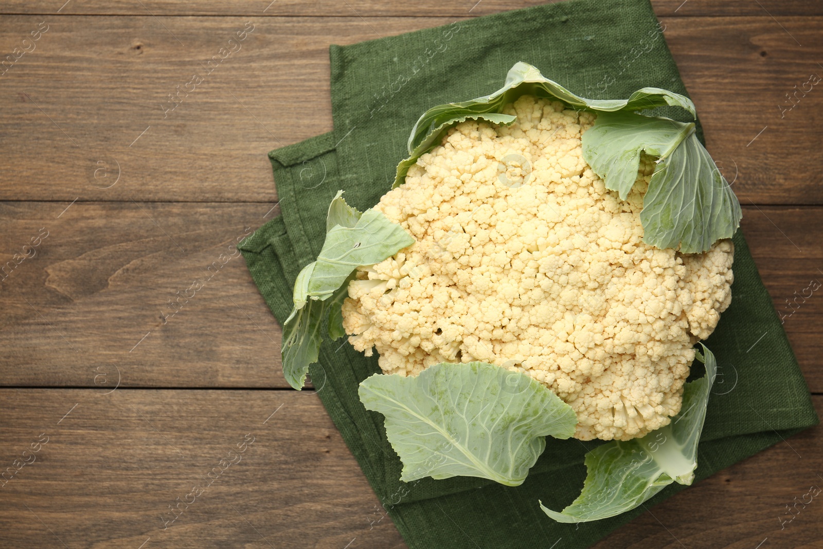 Photo of Fresh cauliflower with green leaves on wooden table, top view. Space for text